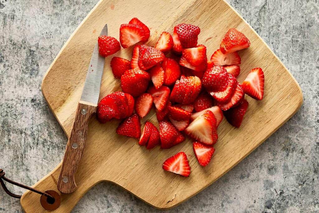 a top down view of a wooden chopping board and strawberries cut into wedges with a small pairing knife - 13