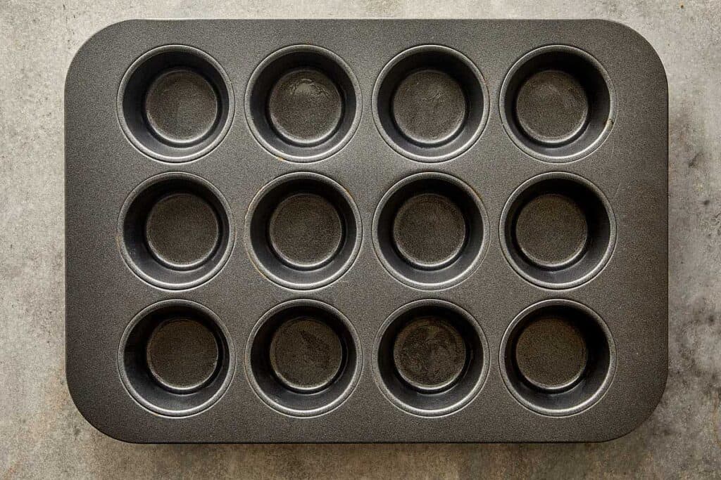 A top down view of a muffin tray non stick dark grey with 12 holes - 3