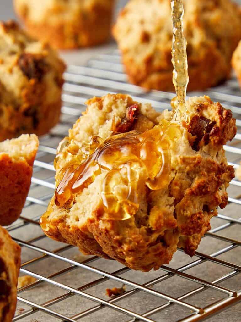 a close up side shot of a muffin on a wire rack cooling with honey being poured over it - 1