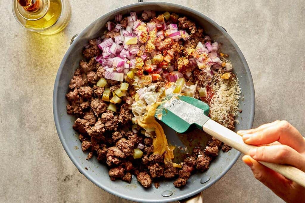 a top down view of a pan filled with mince meat being cooked on a benchtop stove, there is onions and garlic inside now - 7