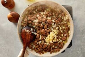 overtop view of garlic, onion and beef being mixed in a beige pan
