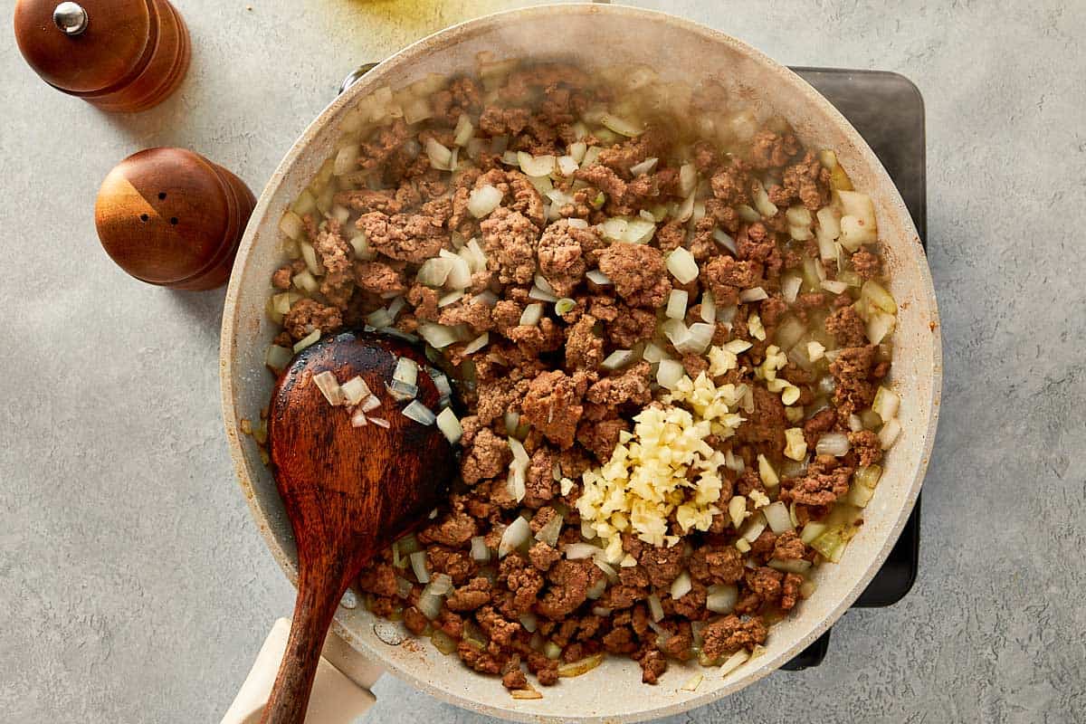 top overview of garlic, onion and beef being mixed in a beige pan - 7
