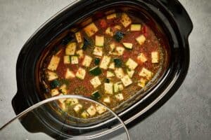 Slow cooker filled with lasagna soup ingredients, including zucchini, tomato base, and herbs, ready to cook