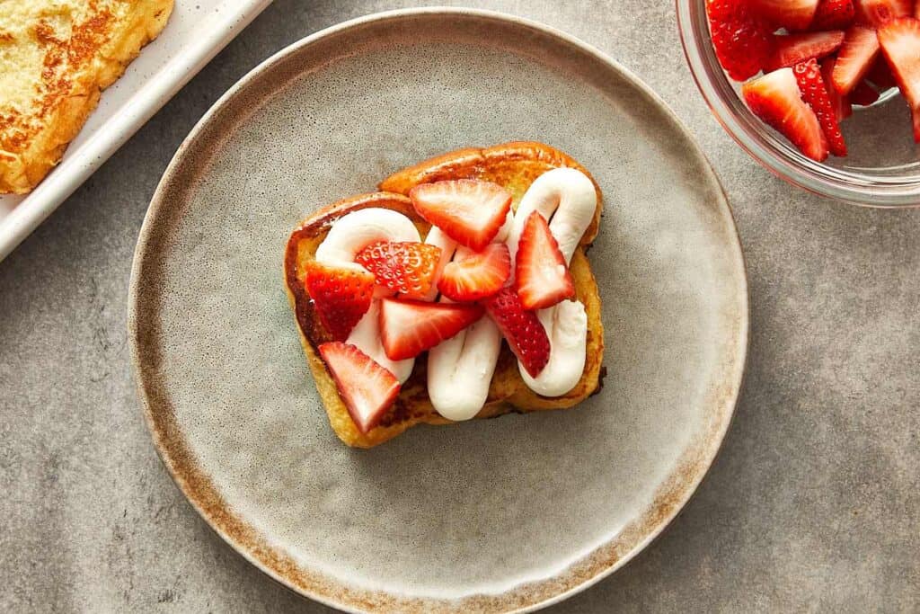 slices of strawberries sitting on top of a slice of brioche toast with cream in the middle.