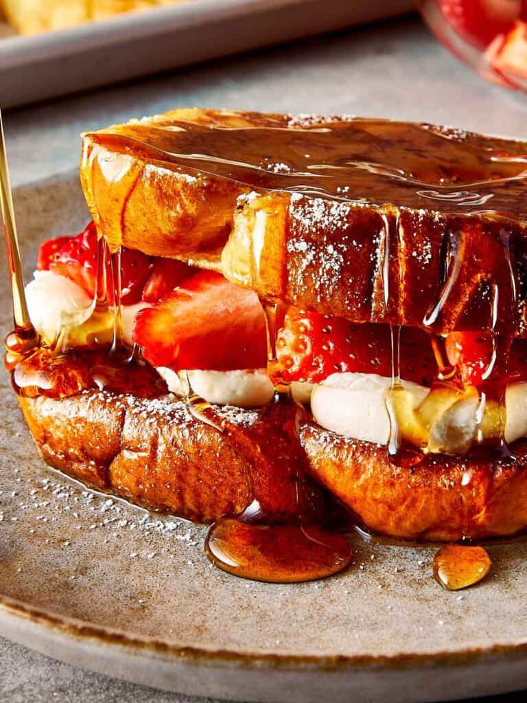 a close up of brioche toast with strawberries and white frosting in the middle, covered in maple syrup