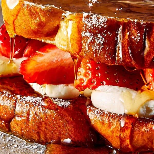 a close up shot a close up of brioche toast with strawberries and white frosting in the middle, covered in maple syrup
