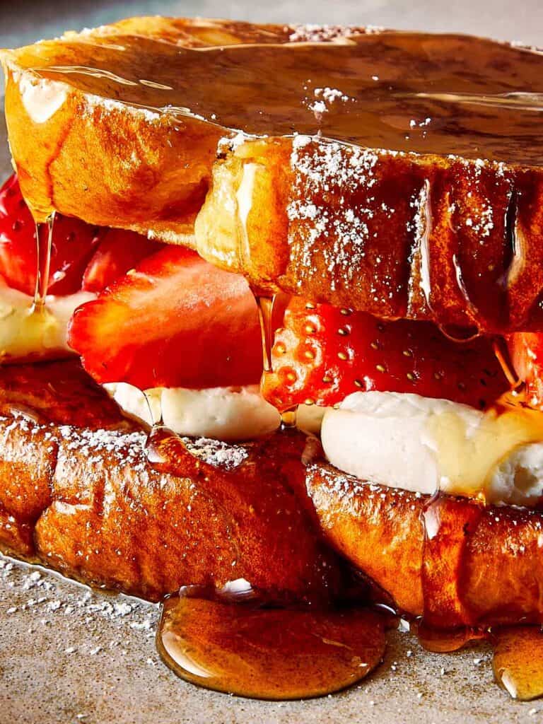 a close up shot a close up of brioche toast with strawberries and white frosting in the middle, covered in maple syrup