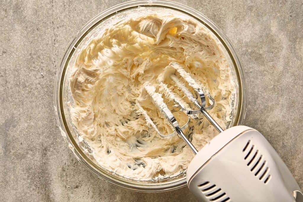a top down view of an electric hand mixer with cream cheese frosting being mixed together.