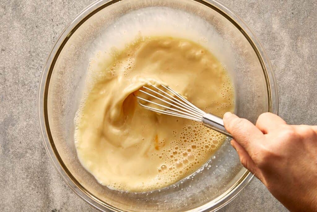 a glass bowl with a hand mixing the eggs and milk with a wire whisk