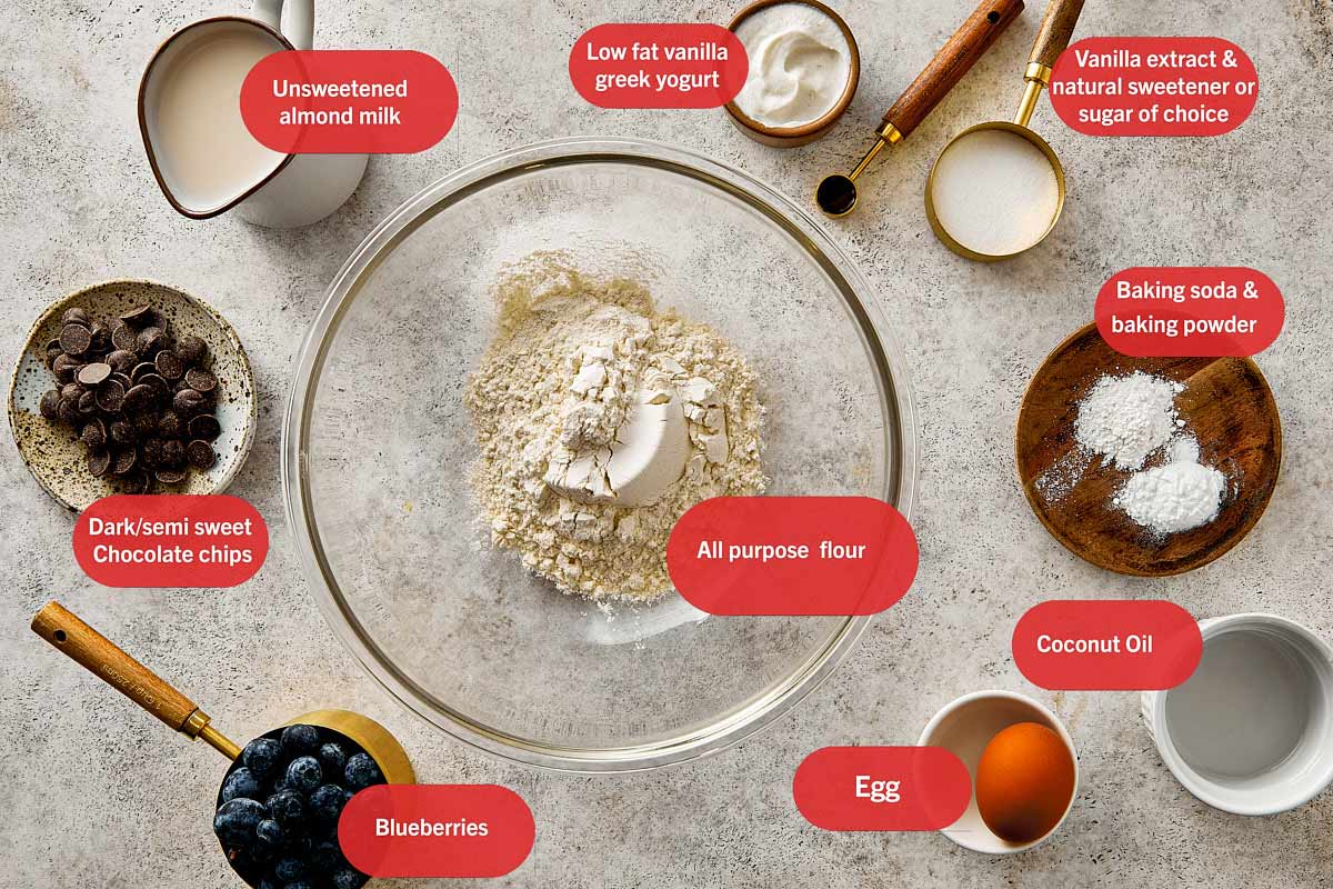 top overview of the ingredients for blueberry pancakes. Including Almond milk, vanilla Greek yogurt, vanilla extract, baking soda, baking powder, egg, coconut oil, blueberries, dark chocolate chips, and all-purpose flour.