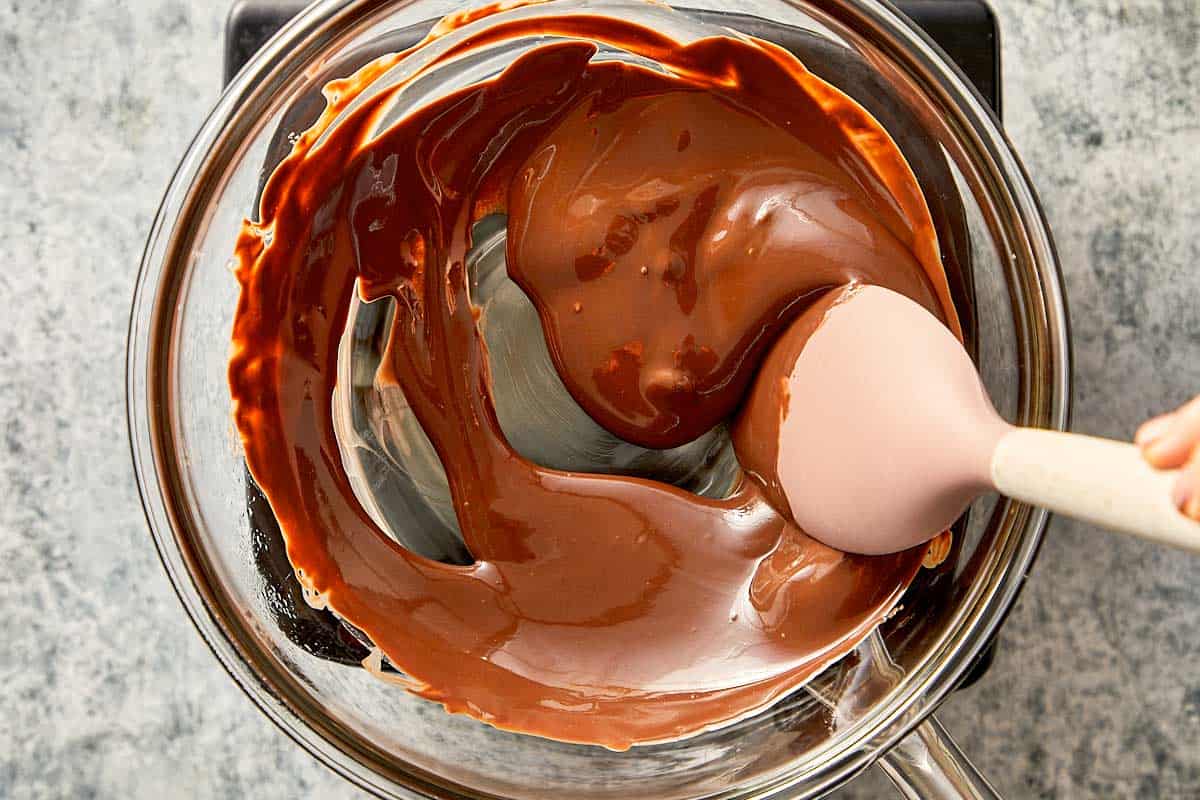 Top overview of melted chocolate in a bowl, being gently mix with a plastic spoon.