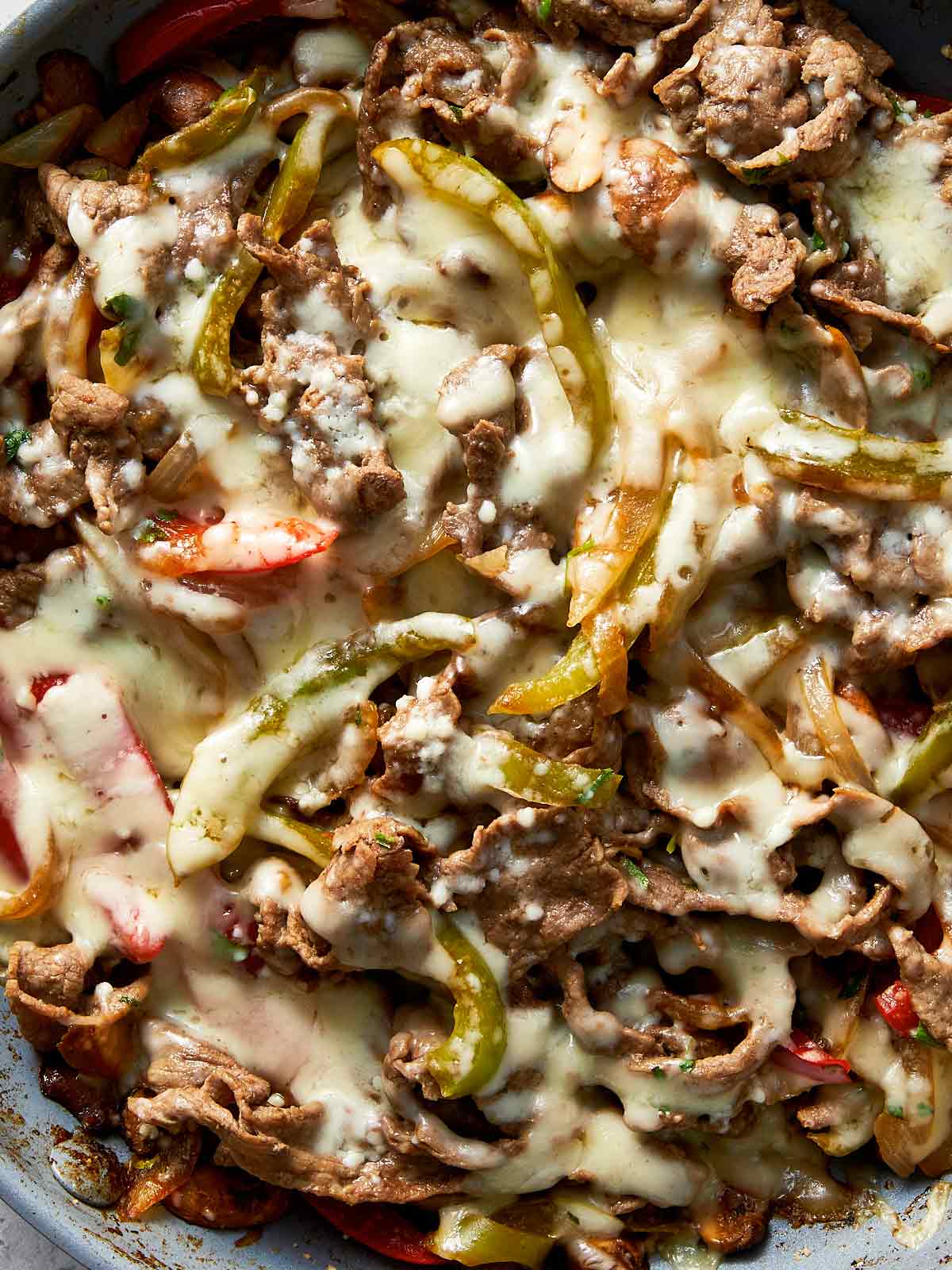 One pan Philly cheesesteak skillet with thinly sliced steak, sautéed peppers and onions, and melted mozzarella cheese bubbling on top.