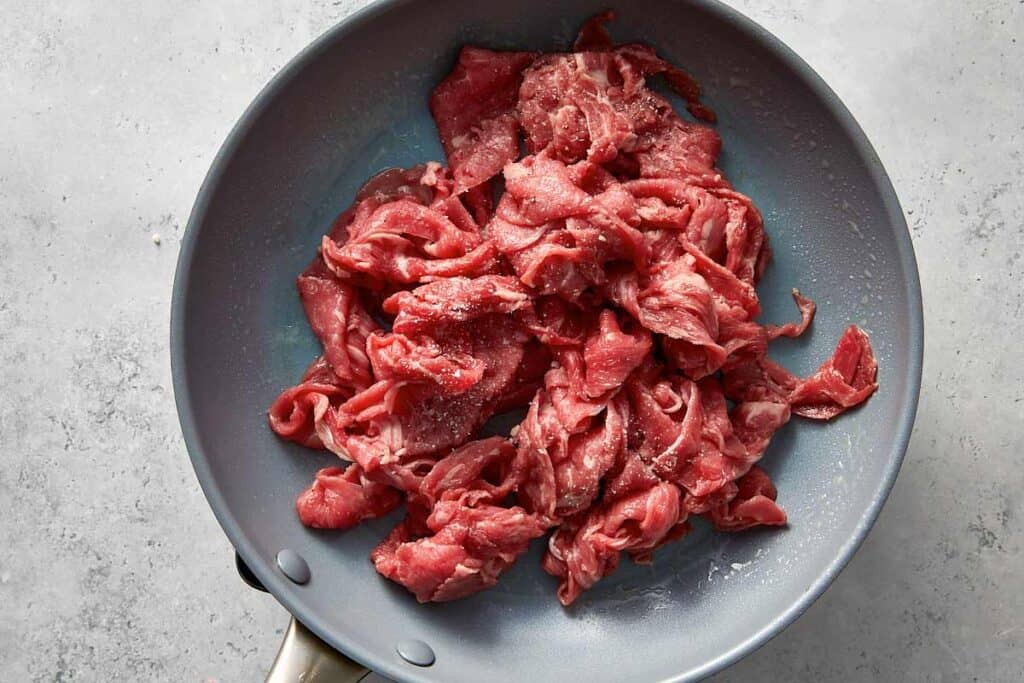 Thinly sliced sirloin steak added to a hot nonstick skillet and seasoned with salt and black pepper.