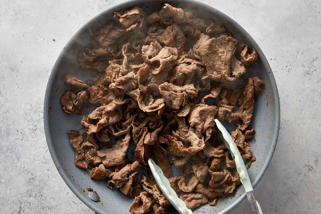 Thinly sliced steak browning in a nonstick skillet, cooked quickly over high heat until just seared and tender.