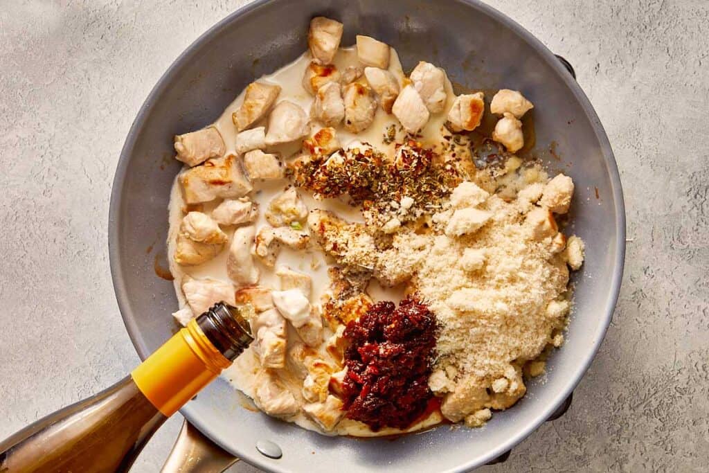 a top down view of chicken and cream and spices all in one ready to mix. There is a wine bottle pouring wine into the pan and it is frying.