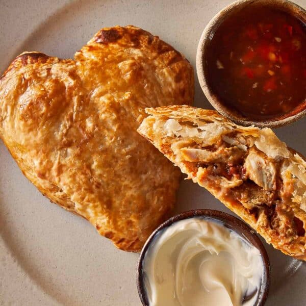 A top down view of a heart shaped tart and a half hart tart sliced in 2 with marry me chicken stuffing inside. A tomato sauce relish in a jar on the side.