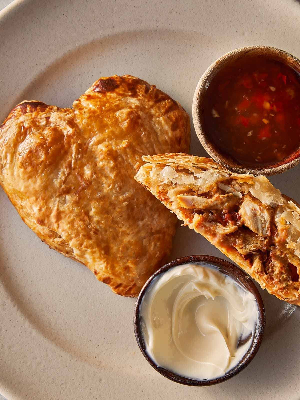 A top down view of a heart shaped tart and a half hart tart sliced in 2 with marry me chicken stuffing inside. A tomato sauce relish in a jar on the side.