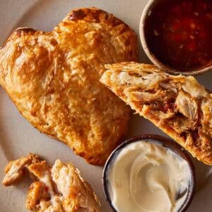 A top down view of a heart shaped tart and a half hart tart sliced in 2 with marry me chicken stuffing inside. A tomato sauce relish in a jar on the side.