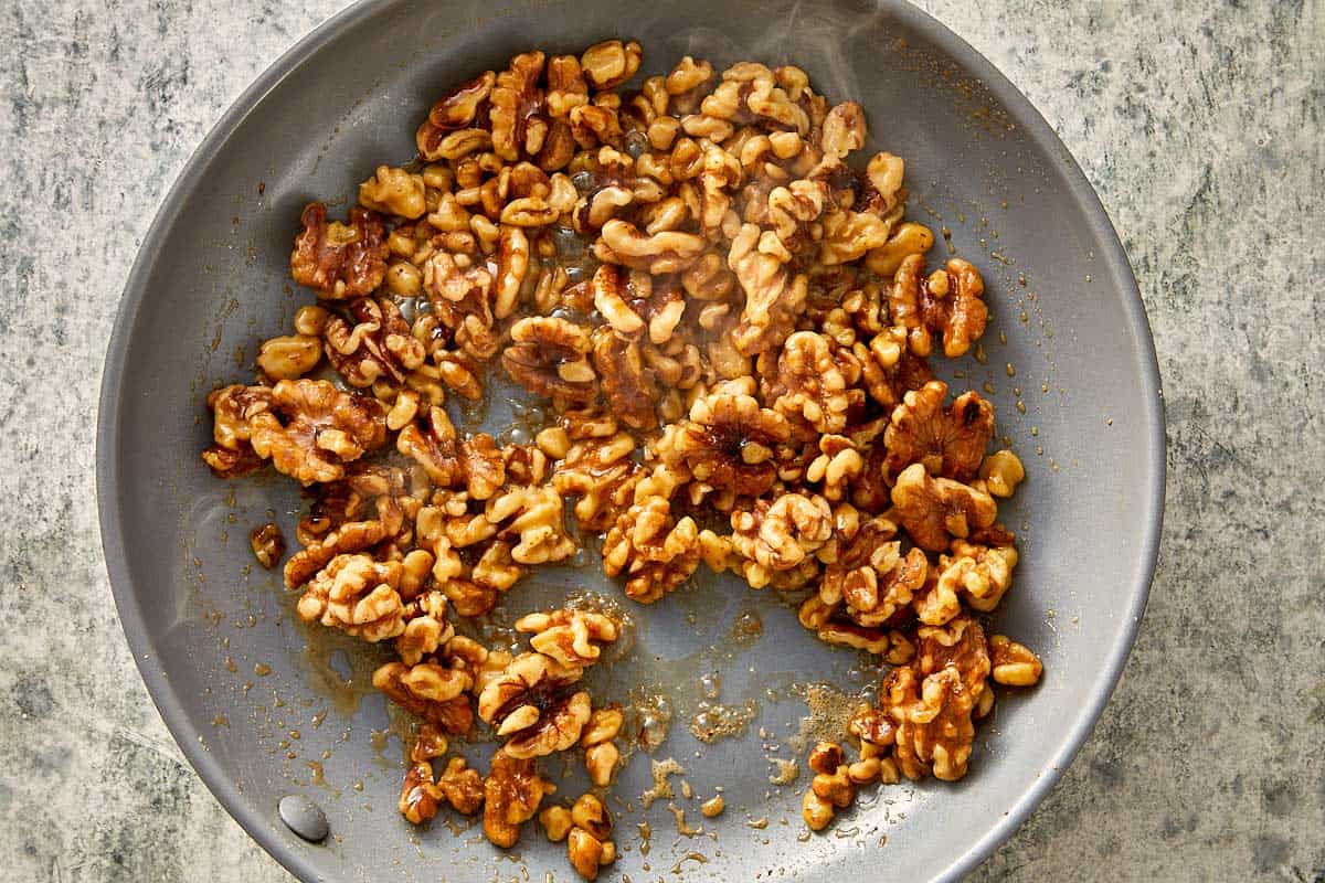 Maple-glazed walnuts caramelizing in a nonstick skillet for arugula salad, lightly toasted until golden and glossy.