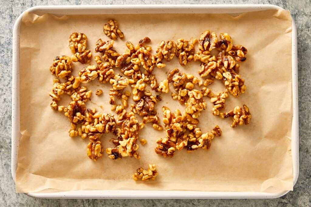 Maple-glazed walnuts cooling on a parchment-lined baking tray after toasting.