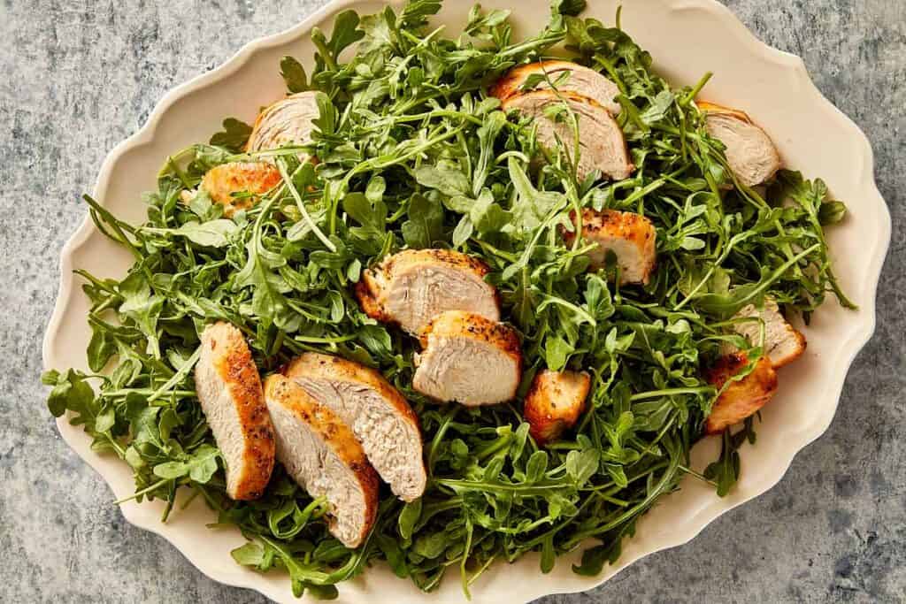 Fresh arugula salad with sliced grilled chicken, ready to be assembled with toppings.