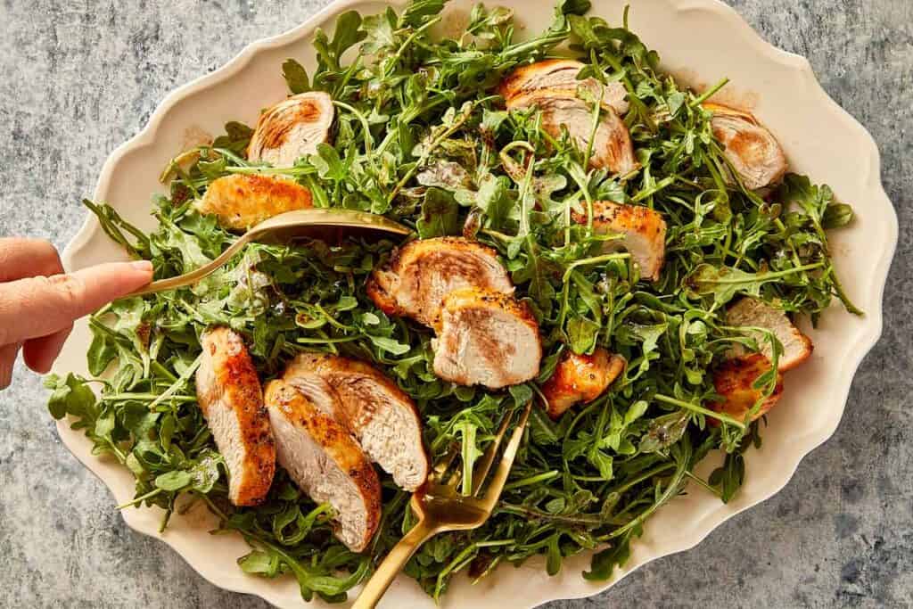 Grilled chicken and arugula salad being gently tossed with dressing before serving.