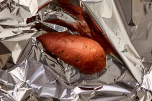 Whole sweet potato wrapped in foil, unpeeled and ready to roast in the oven.