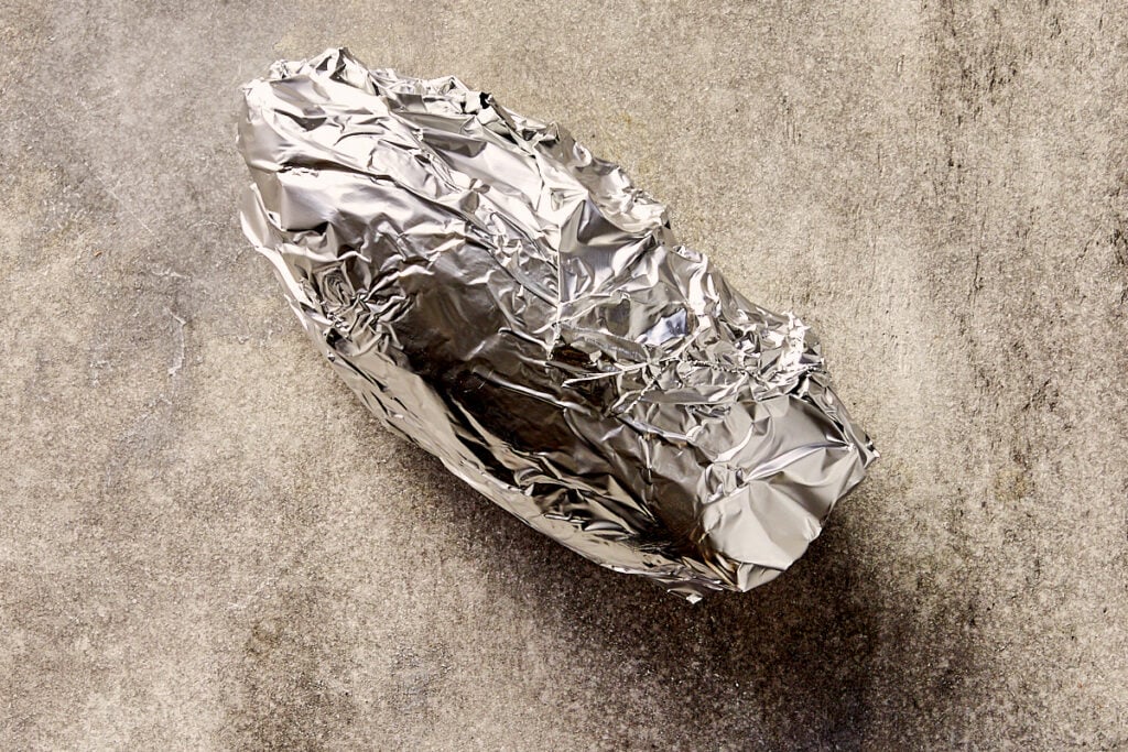 Whole sweet potato wrapped in foil, unpeeled and ready to roast in the oven.