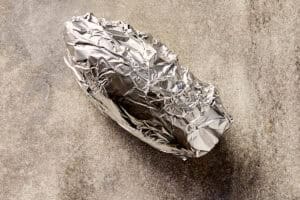 Whole sweet potato wrapped in foil, unpeeled and ready to roast in the oven.