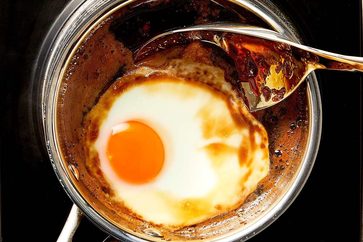 Top overview of poached egg being removed from the homemade teriyaki sauce