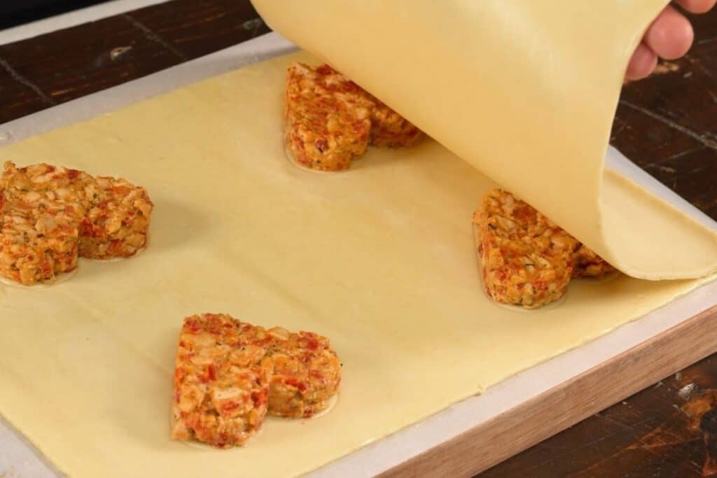 two sheets of puff pastry with chicken meat filling being placed together