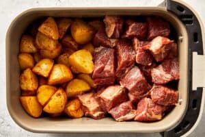 Top overview of potatoes and raw steak in the air-fryer