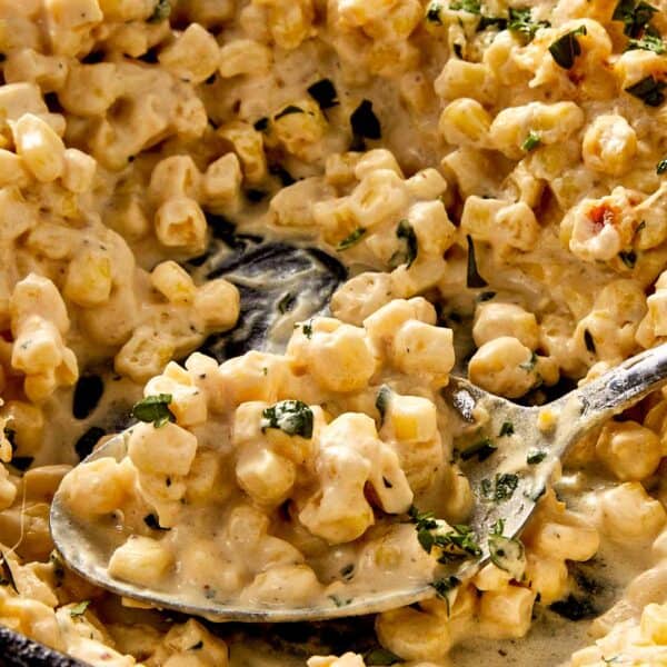 Creamy corn with melted parmesan and fresh parsley, scooped from a pan with a spoon