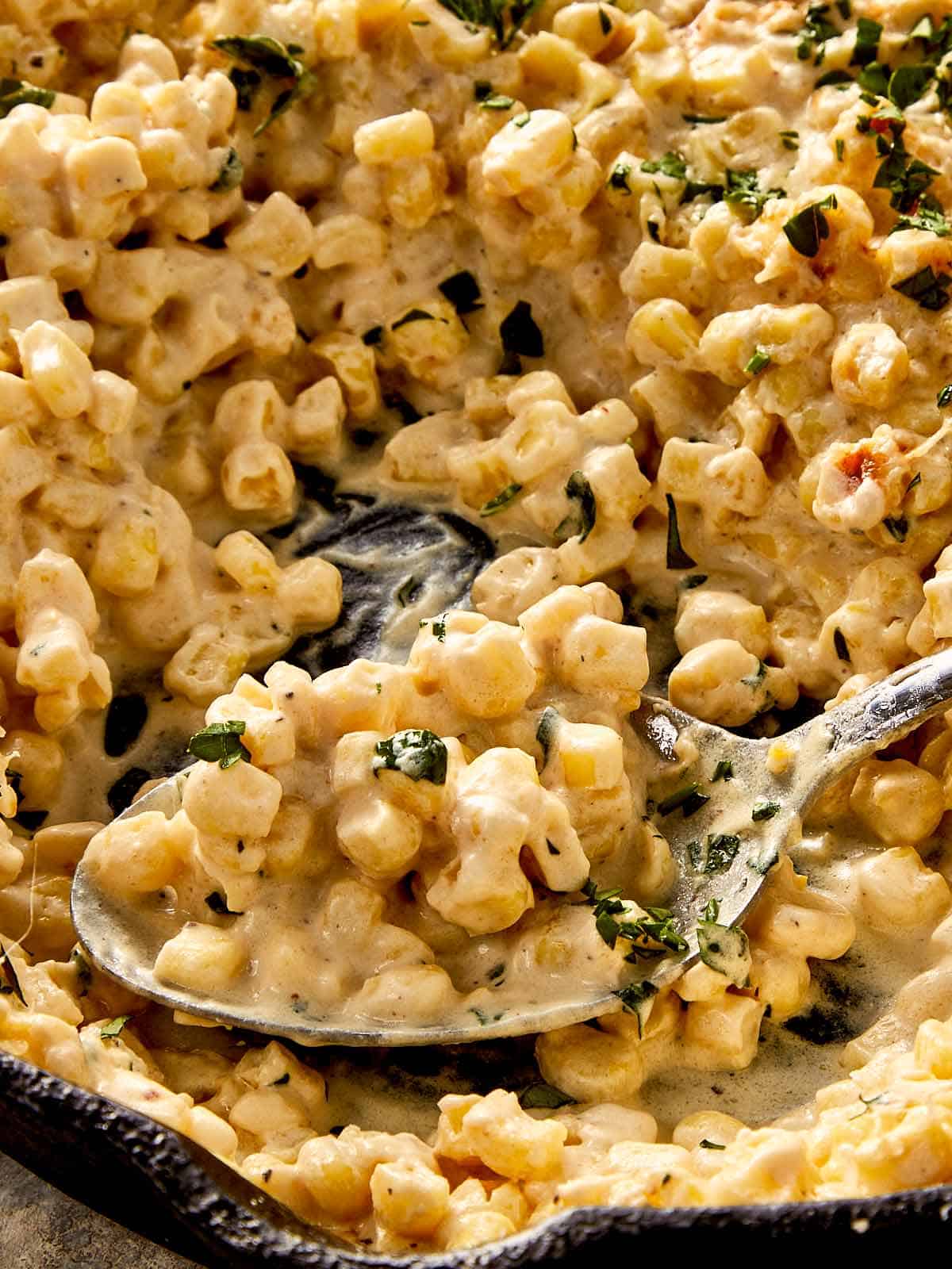Creamy corn with melted parmesan and fresh parsley, scooped from a pan with a spoon