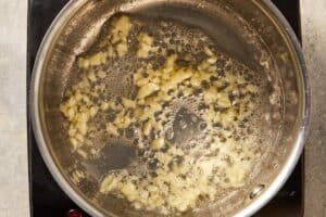 Minced garlic cooking in melted butter in a pan, becoming fragrant for creamy corn recipe