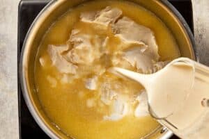Light cream being poured into a pan with cream cheese and chicken stock to create a smooth base for creamy corn