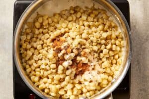 Frozen corn added to a creamy base with salt, black pepper, sugar, and nutmeg, ready to simmer until tender