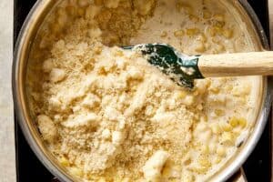 Grated parmesan being added to creamy corn mixture, ready to melt and thicken the sauce