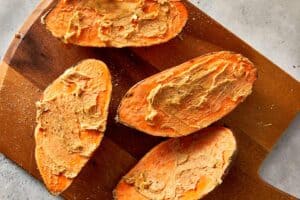 Baked sweet potatoes cut open and spread with garlic butter on a wooden board