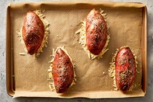 Baked sweet potatoes topped with grated Parmesan on a lined baking tray, ready to go into the oven