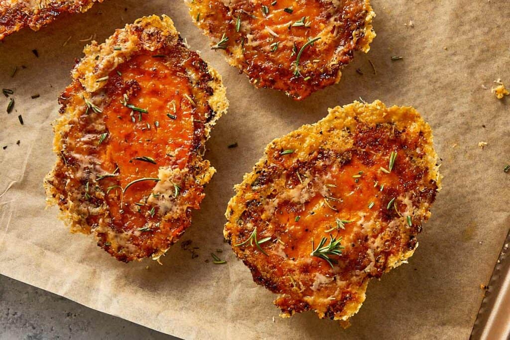Crispy baked sweet potatoes with melted Parmesan and herbs on a lined baking tray