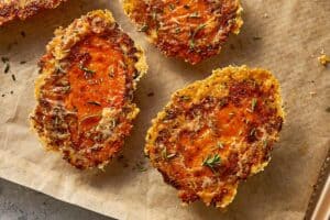 Crispy baked sweet potatoes with melted Parmesan and herbs on a lined baking tray