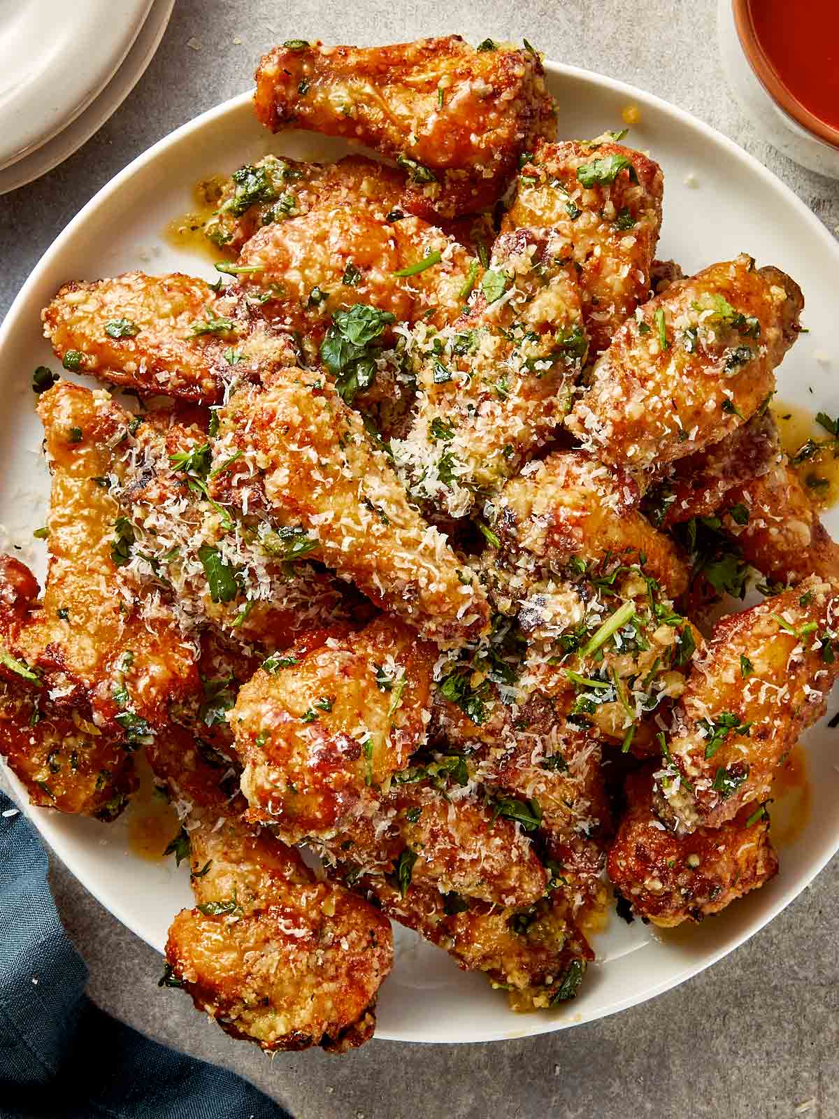 crispy garlic parmesan chicken wings coated in garlic butter, parmesan and herbs, served on white plate