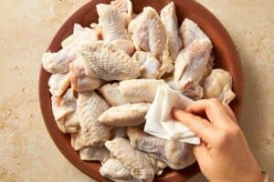 Patting raw chicken wings dry with paper towels before seasoning to help them crisp up when cooking