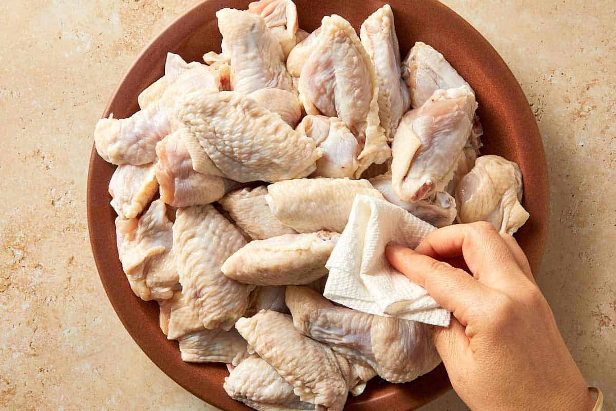 Patting raw chicken wings dry with paper towels before seasoning to help them crisp up when cooking