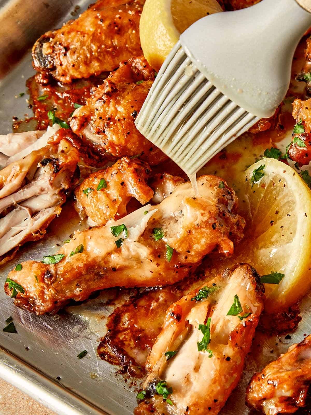 Crispy lemon pepper chicken wings coated in butter sauce, garnished with parsley and served with lemon wedges