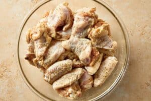 Raw chicken wings tossed with lemon pepper seasoning and baking powder in a bowl, evenly coated before cooking