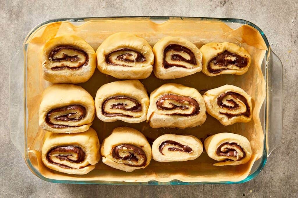 Unbaked Nutella rolls placed in a lined baking dish