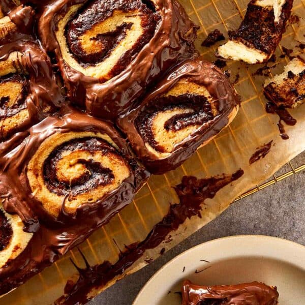 Freshly baked Nutella rolls topped with melted chocolate spread, arranged on parchment paper with visible swirls and soft texture