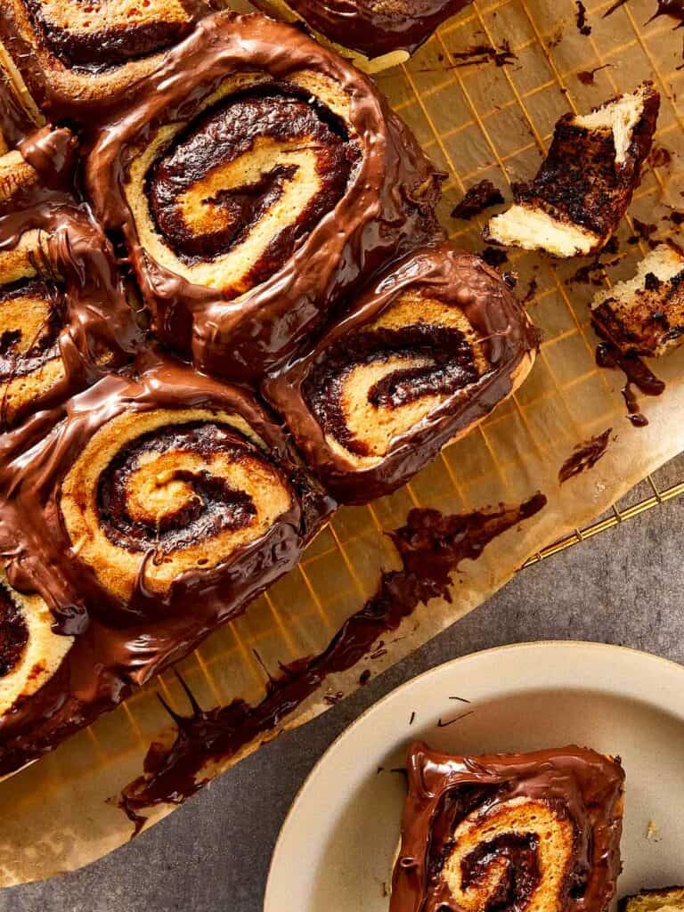 Freshly baked Nutella rolls topped with melted chocolate spread, arranged on parchment paper with visible swirls and soft texture